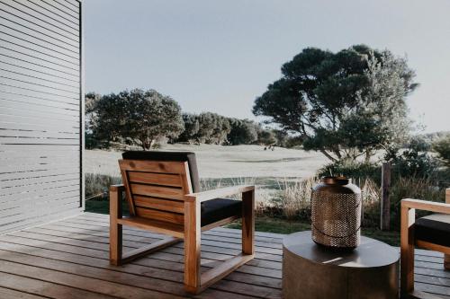 a wooden chair on a porch with a view of a golf course at Bangalay Luxury Villas in Shoalhaven Heads