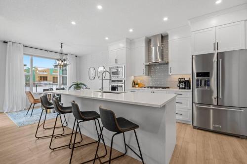 a kitchen with white cabinets and a large island with bar stools at Luxury-4bed with AC-86"TV-BrandNew in Cranston, Calgary in Calgary