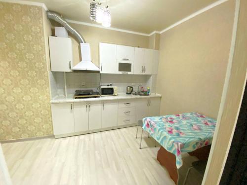 uma pequena cozinha com armários brancos e uma mesa em apartment near Cosmopark complex em Bishkek