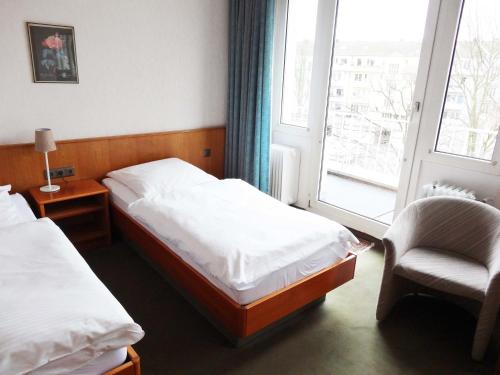 a bedroom with two beds and a chair and a window at Zentral Hotel Poststuben in Krefeld
