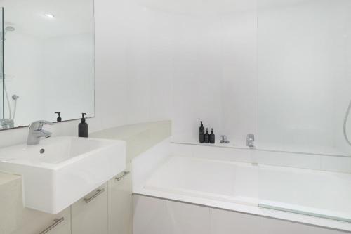 Baño blanco con lavabo y espejo en The Cove Noosa - Apartment 16, en Noosa Heads