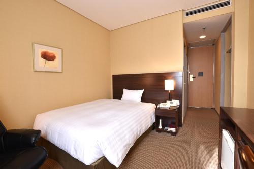 a hotel room with a large bed and a chair at Hotel Nikko Tsukuba in Tsukuba