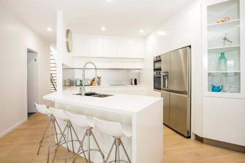 a white kitchen with a counter and stools at Bowers Nest Pet Friendly 2 Mins Walk to Beach in Culburra Beach