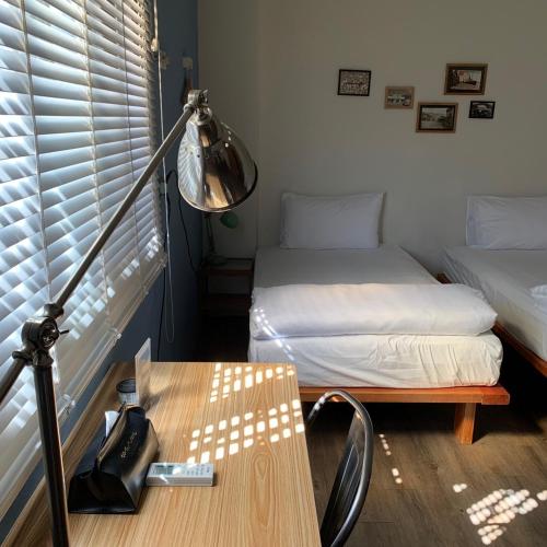 a room with two beds and a desk with a lamp at Cozy House Hostel in Hualien City