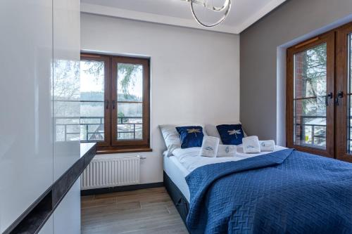 a bedroom with a bed with blue sheets and windows at Green Park Resort B1- z dostępem do basenu, sauny, jacuzzi, siłowni in Szklarska Poręba