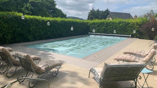 a swimming pool with chairs and a table at Amber Cottage in Little Witcombe