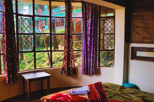 a bedroom with windows and a bed and a table at kailwood Guest House in McLeod Ganj