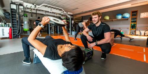 a man helping a woman do pushups in a gym at Maashof in Venlo