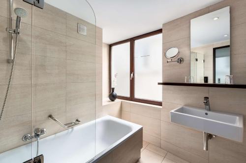 La salle de bains est pourvue d'une baignoire, d'un lavabo et d'un miroir. dans l'établissement NH Brussels Grand Place Arenberg, à Bruxelles