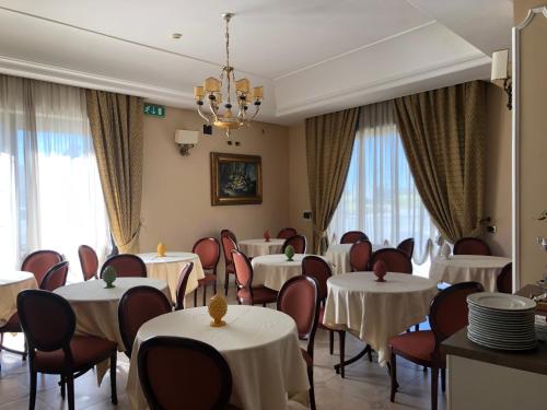 un restaurante con mesas y sillas blancas y ventanas en D'Angelo Palace Hotel, en Mazara del Vallo