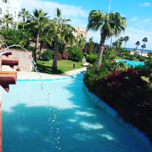 a swimming pool with blue water and palm trees at Marina Smir Hotel & Spa in M'diq