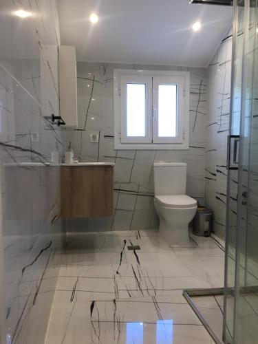 Łazienka wyłożona jest białymi kafelkami i dysponuje toaletą oraz oknem. w obiekcie Άνετο και πολυτελές οροφοδιαμέρισμα 2 w Chanii