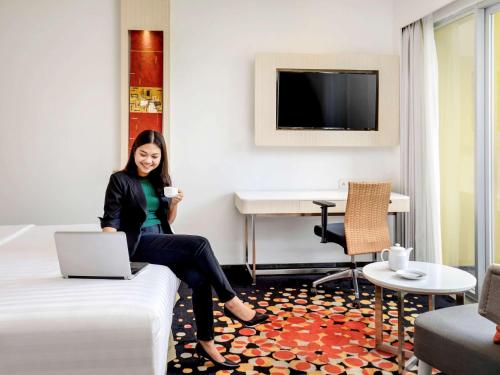 a woman sitting on a bed in a hotel room at Novotel Palembang in Palembang