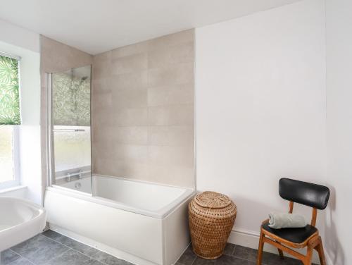 a white bathroom with a tub and a chair at Gwynant - Morfa Nefyn in Pwllheli