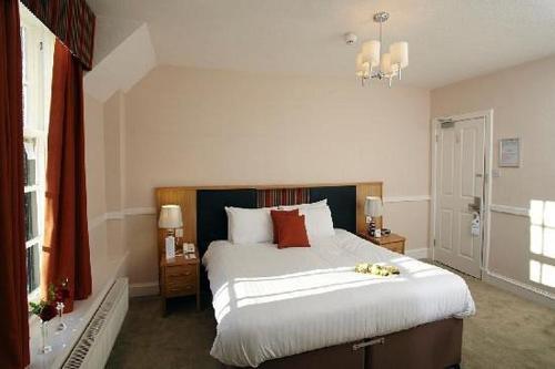 um quarto com uma cama grande com lençóis brancos e almofadas vermelhas em Buchanan Arms Hotel & Leisure Club em Drymen
