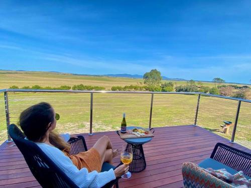 a woman sitting on a deck with a glass of wine at Wamoon Retreat - Luxe House in Yanakie