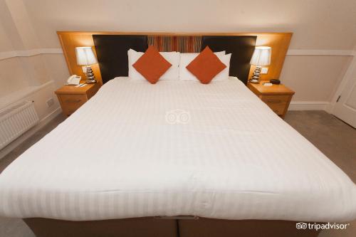 1 dormitorio con 1 cama blanca grande con almohadas de color naranja en Buchanan Arms Hotel & Leisure Club, en Drymen