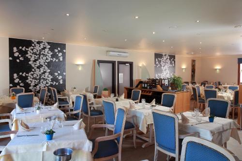 a restaurant with white tables and blue chairs at Logis Le Luth in Mirecourt