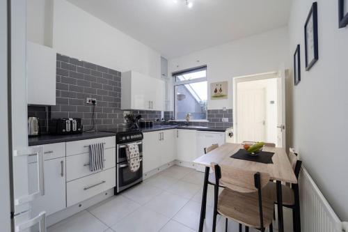eine Küche mit weißen Schränken und einem Holztisch in der Unterkunft Modern Flat in Porthcawl in Porthcawl