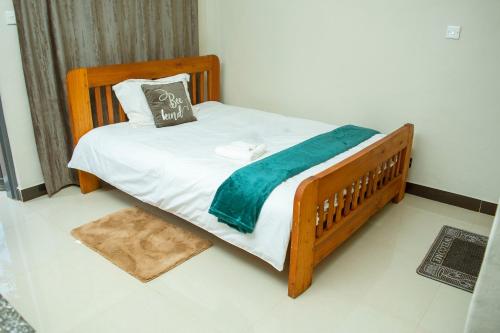 ein Holzbett mit einer blauen Decke und einem Kissen in der Unterkunft Avon Garden Apartments Area 25 in Lilongwe