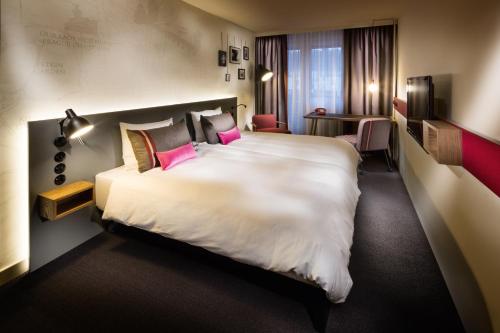Cette chambre comprend un grand lit blanc avec des oreillers roses. dans l'établissement pentahotel Paris Charles de Gaulle, à Roissy-en-France