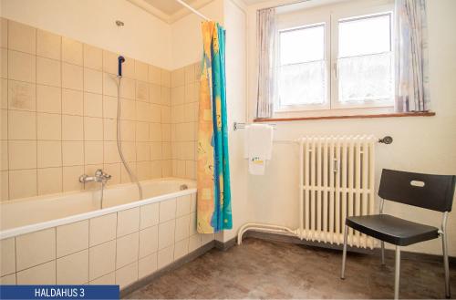 een badkamer met een bad, een stoel en een raam bij Haus Haldahus by Arosa Holiday in Arosa