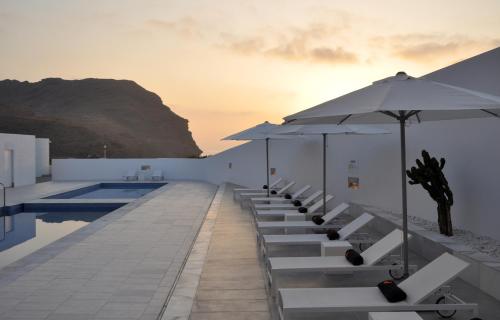 a row of white chairs with umbrellas and a pool at Hotel Spa Calagrande Cabo de Gata in Las Negras