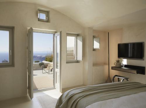 a bedroom with a bed with a television and a balcony at Atoles Retreat in Imerovigli