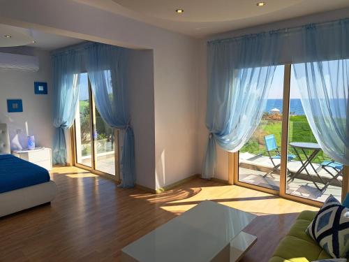 Schlafzimmer mit blauen Vorhängen und einem großen Glasfenster in der Unterkunft Villa Sunshine in Mazotos