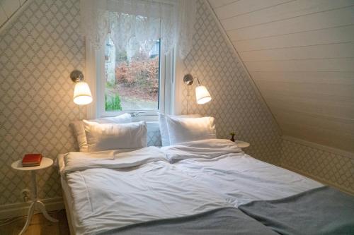 a bed with white sheets and pillows in a room with a window at Anfasteröd Gårdsvik - badstugor med loft in Ljungskile