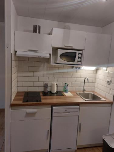 une cuisine avec des armoires blanches, un évier et un micro-ondes dans l'établissement Appartement comme à la maison, à Bourbonne-les-Bains