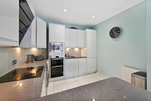伦敦Hampstead Opulence Apartment - Luxurious Split Level Property的厨房里有白色的橱柜，墙上挂着一个钟