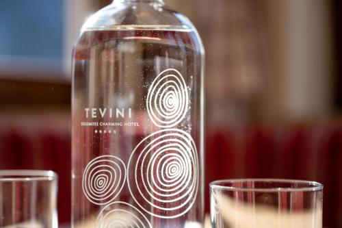 a glass bottle with a swirl on it with two glasses at Tevini Dolomites Charming Hotel in Commezzadura
