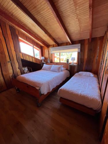 two beds in a wooden room with two windows at Kumewe Lodge in Panguipulli