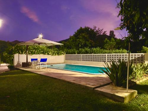 a swimming pool with an umbrella and two chairs and a table at Seu Refúgio Rural Piscina Privativa e Natureza in Tubarão