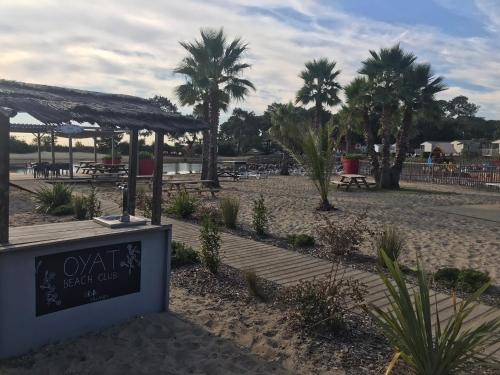 a beach with tables and palm trees and a sign at Chris et Sabrina - Camping Les Viviers 4 étoiles in Lège-Cap-Ferret