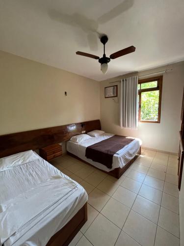 1 dormitorio con 2 camas y ventilador de techo en DE FRENTE PRA PRAIA Apartamento da Cris Taperapua - Condomínio América Praia Flat, en Porto Seguro