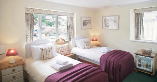 a bedroom with two beds and a tv and windows at The Old Bridge House in Looe
