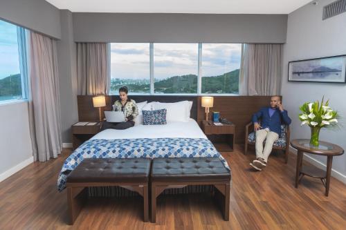 two people sitting in a hotel room with a bed at Golden Tulip Porto Vitória in Vitória