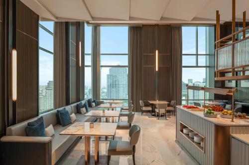 a restaurant with tables and chairs and large windows at Le Meridien Bangkok in Bangkok