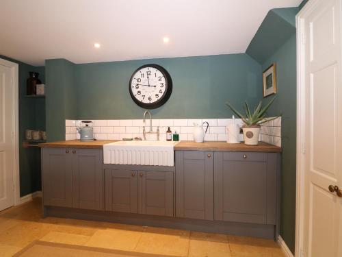 a kitchen with a sink and a clock on the wall at Pudding Hill Barn Cottage in Cirencester