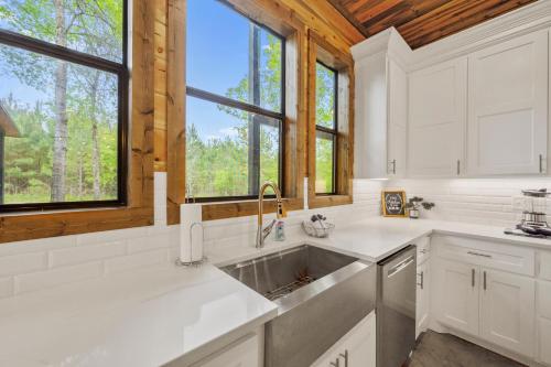 a kitchen with white cabinets and a sink and windows at Fun & Inviting Modern Luxury 4br Retreat At Broken Bow Lake Features Hot Tub, Fire Pit, Playground And More Once In A Blue Moon By Boutiq in Broken Bow