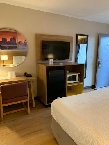 a hotel room with a bed and a desk and a television at Days Inn by Wyndham Louisville Airport Fair and Expo Center in Louisville