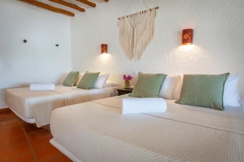 two beds in a room with white walls and green pillows at Beachfront Hotel La Palapa - Adults Only in Holbox Island
