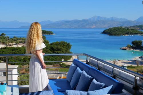 a woman standing on a balcony looking out at the water at Hotel Ajden by Mira Mare in Ksamil