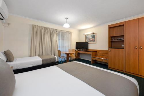 a hotel room with two beds and a desk at Pegasus Motor Inn and Serviced Apartments in Brisbane