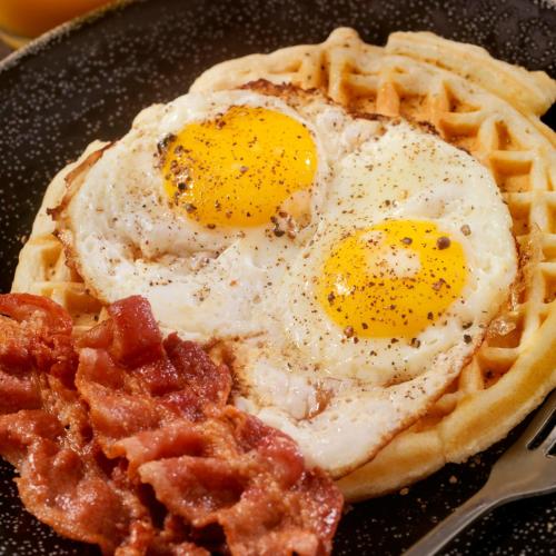 two eggs on top of a waffle with bacon at Hotel Le Paris in Noumea