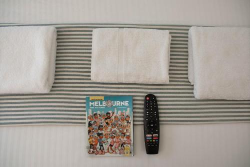 a remote control and a book on a bed with towels at Nomads St Kilda in Melbourne