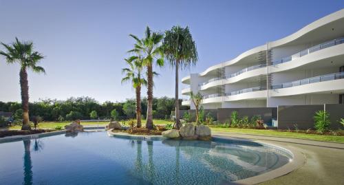 a swimming pool in front of a building with palm trees at Cotton Beach Resort - Tweed Coast Holidays ® in Kingscliff