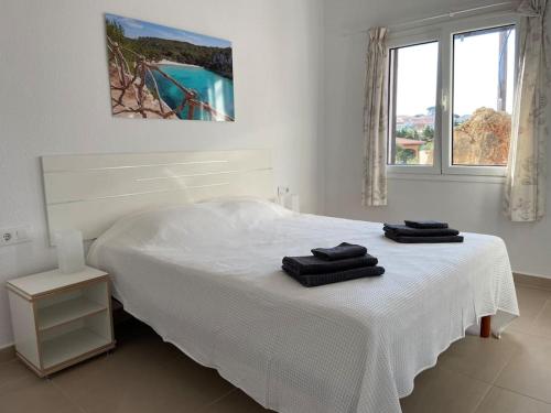 a white bedroom with a bed with two towels on it at Modernes Apartment mit traumhaftem Blick Vistamar3 in Cala'n Porter